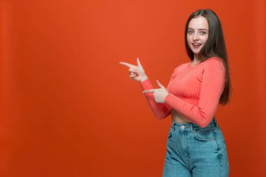 Boş fotokopi alanını gösteren mutlu genç kız turuncu arka planda reklam için yer gösteriyor.