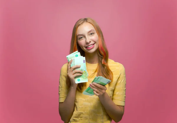 Happy bohatá mladá dívka s penězi, těší peníze vítězství, velký zisk a bohatý život na růžové pozadí studia — Stock fotografie