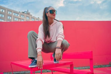 Havalı stil sahibi genç bir kız şehirdeki açık hava masasında kablosuz kulaklıkla rap müzik dinliyor. Kentsel yaşam tarzı