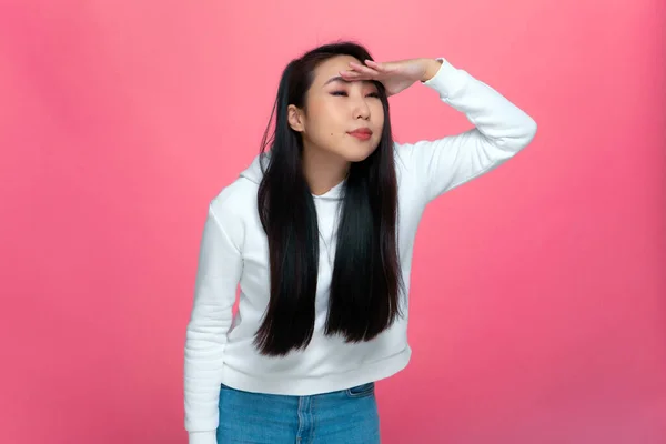 Fokuserad ung asiatisk flicka tittar långt borta med hand över huvud, söker på rosa studio bakgrund. Begreppet framtidsplaner — Stockfoto