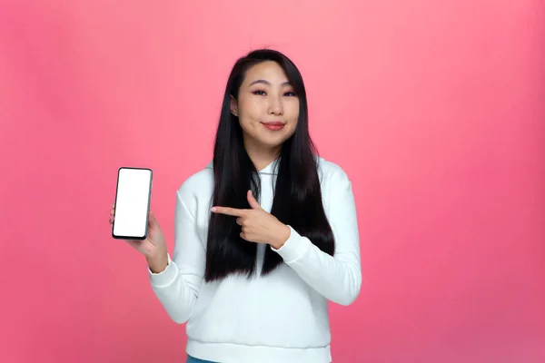 Bella moderna ragazza asiatica che mostra smartphone con schermo bianco vuoto per l'annuncio, raccomandando nuove applicazioni — Foto Stock