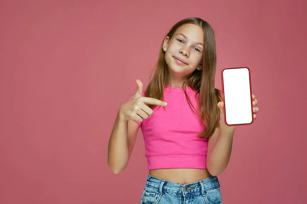 Ragazzina sorridente punto bambino al telefono con schermo bianco, pubblicizzare offerta negozio online bambino o app mobile per bambini — Foto Stock