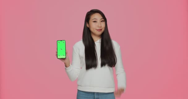 Oferta móvil. Feliz joven asiática chica apuntando en verde maqueta de teléfono de pantalla, mostrando el pulgar hacia arriba gesto, recomendar nueva aplicación — Vídeos de Stock