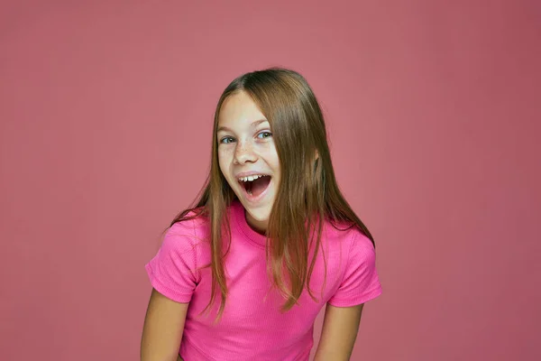 Boldog pozitív kilépett aranyos kislány gyermek nyitott szájjal, grimaszoló, sikoltozó wow rózsaszín stúdió háttér — Stock Fotó