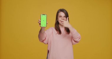 Modern mobil uygulama reklamcılığı. Genç kız, sarı stüdyo arka planında yeşil ekran maketini işaret ediyor.