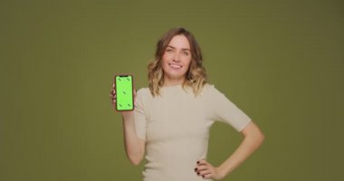 Mutlu genç kadın yeşil ekranlı telefonu gösteriyor. Kız modern mobil uygulama, indirimler, ucuz uçuş biletleri öneriyor.