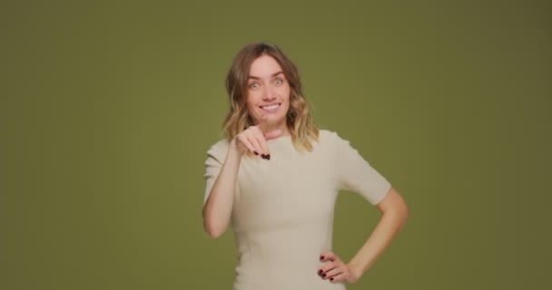 Красива усміхнена жінка, що показує мені жест пальцями, пропонує спілкування на зеленому студійному фоні — стокове відео