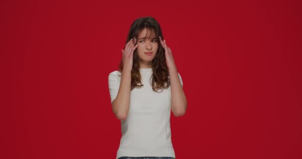 Больные грустные молодые девушки массажные виски страдают головной болью, болезненными чувствами, мигренью на фоне красной студии — стоковое видео