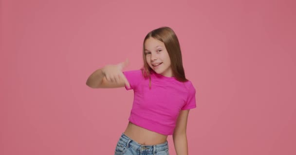 Cute girl child point fingers below, show profitable sale offer, subscription like button on pink studio background — Stock Video