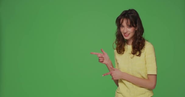 Lächelndes junges Mädchen zeigt mit den Fingern zur Seite auf Kopierraum auf chromakeygrünem Hintergrund für moderne Werbung — Stockvideo