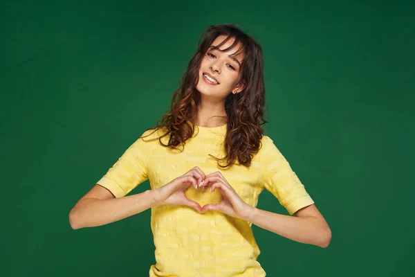 Szívből jövő gesztus. Hálás fiatal lány mutatja szerelem jel zöld stúdió háttér. Jótékonysági és adományozási koncepció. — Stock Fotó