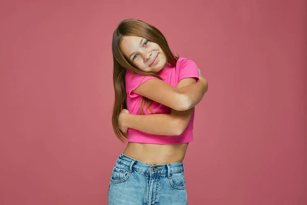 Leende barn flicka omfamna sig på rosa bakgrund. Kärlek och självacceptans. Friska barn självkänsla — Stockfoto