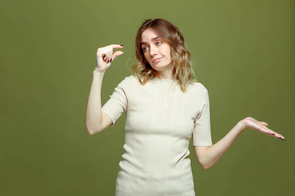 Insatisfeito jovem mulher mostrar pequeno tamanho gesto por dedos, espalhar as mãos no fundo do estúdio verde — Fotografia de Stock