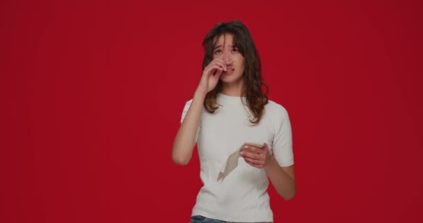 Doente bela menina espirrando em tecido, sofrendo de corrimento nasal, sintomas de combustão ou alergia em fundo estúdio vermelho — Vídeo de Stock