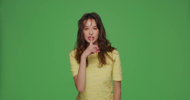 Beautiful young girl show silence gesture ask to be quiet, keep secret on chromakey green background. Privacy concept — Stock Video