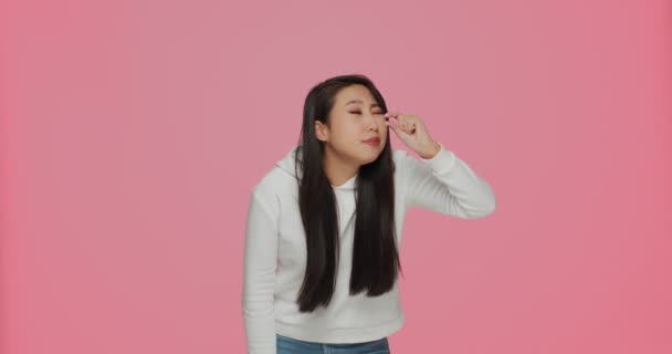 Расстроенная молодая азиатская девушка показывает пальцами жест малого размера, мало измерений на розовом фоне студии — стоковое видео