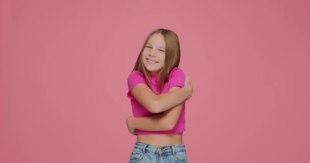 Bella bambina si abbraccia con amore su sfondo rosa studio. Autostima infantile positiva, cura di sé — Video Stock