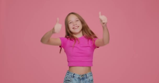Boldog gyermek lány mutatja hüvelykujj fel, elégedett iskoláslány blogger kérni, hogy tegye tetszik, ajánlott szolgáltatás rózsaszín háttér — Stock videók