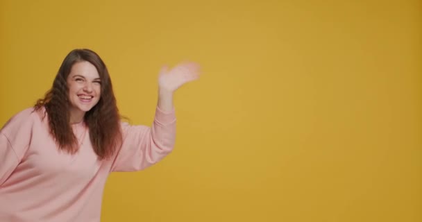 Smiling young girl blogger greeting subscribers wave hand say hello on yellow background with copy space for advertising — Stockvideo