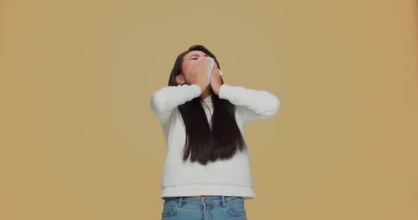 Нездоровая аллергическая азиатка чихает в салфетке, чувствует себя плохо, страдает гриппом на фоне желтой студии — стоковое видео