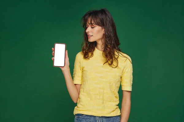 Chica joven moderna mostrando el teléfono mirando en blanco pantalla maqueta. Nuevo entretenido o citas publicidad aplicación móvil — Foto de Stock