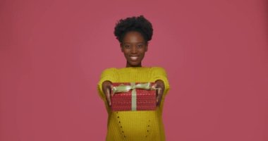 Dost canlısı genç Afrikalı Amerikalı kadın kutlanan hediye paketini kameraya verdi, bayramla kutladı, gülümsedi.
