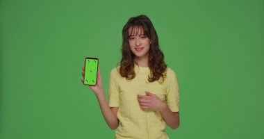 Mobil uygulama reklamı. Güzel, modern bir genç kız kroma tuşundaki yeşil telefon ekranını işaret ediyor.