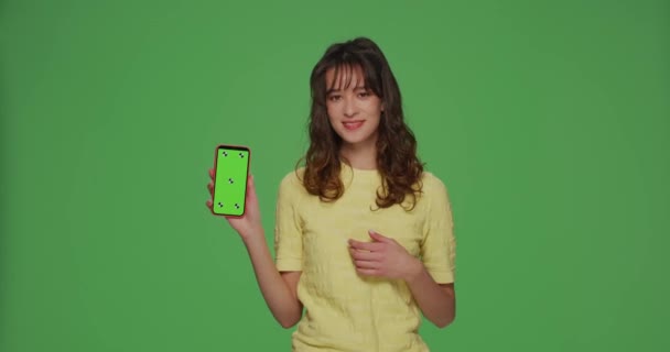 Διαφήμιση εφαρμογών για κινητά. Όμορφη σύγχρονη νεαρή κοπέλα που δείχνει προς το πράσινο mock-up οθόνη του τηλεφώνου στο κλειδί chroma — Αρχείο Βίντεο