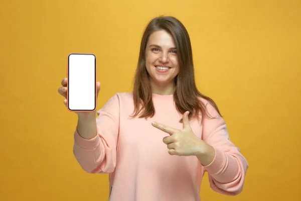 Sonriente joven apuntando con el dedo índice a la pantalla en blanco de la maqueta del teléfono. Anuncio de aplicaciones móviles — Foto de Stock