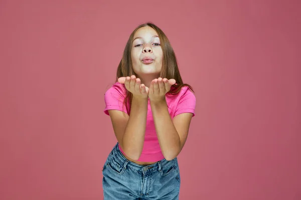 Hermosa niña soplando beso en la cámara, bonita colegiala enviando besos de aire sobre fondo rosa. Amor, gratitud. —  Fotos de Stock