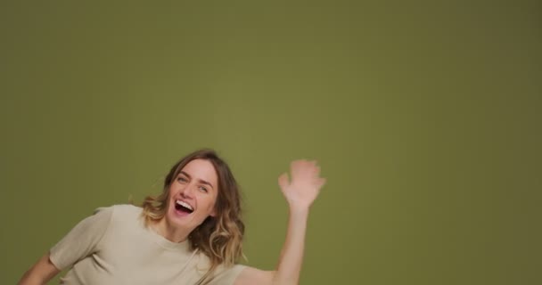 Smiling young woman greeting, wave hand say hello or bye to audience, subscribers, peek out frame on green background — Stockvideo