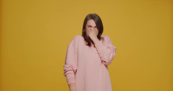 Ung flicka ber att stoppa dålig lukt, hålla andan, nypa näsan, gester för att undvika äcklig doft på gul bakgrund — Stockvideo