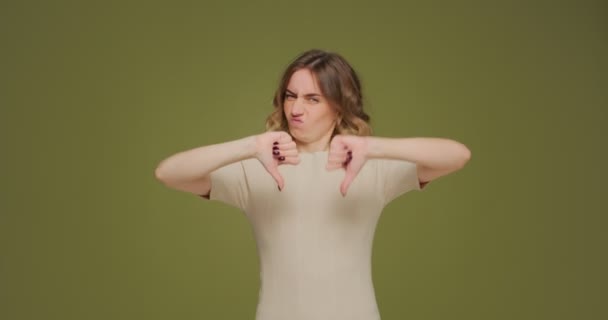 Mécontent jeune femme fronçant les sourcils montrent les pouces de désapprobation vers le bas, détestent signe sur fond vert. Langage corporel — Video