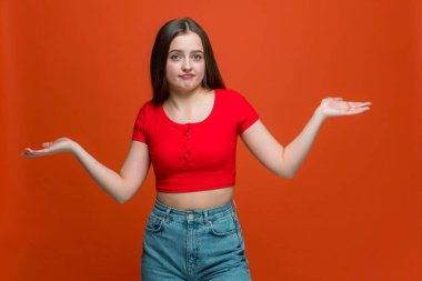 Şaşırmış genç bir kızın omuzlarını silkmesi, zor bir seçimden emin olmaması, turuncu arka planda cevabı bilmemesi.