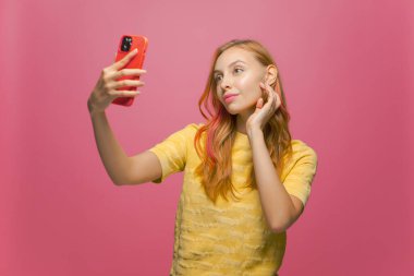 Güzel genç kız telefonda selfie çekiyormuş gibi poz veriyor, güzellik blogcusu sosyal ağ içeriği için kendini fotoğraflıyor.