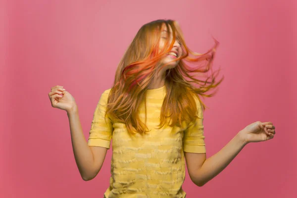 Ganska ung flicka med viftande långt färgat hår njuter av coiffure, har roligt slutna ögon på rosa studio bakgrund — Stockfoto