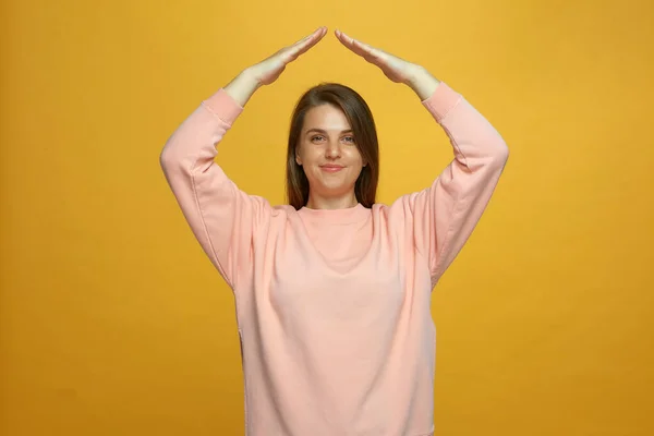 Seguro de vida. positivo jovem menina mostrar casa telhado gesto sobrecarga sentindo-se em segurança no fundo amarelo — Fotografia de Stock