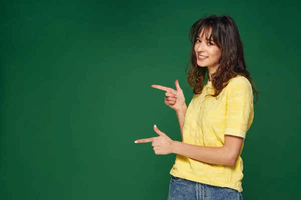 Modern gyönyörű fiatal lány pont-oldalra mutatja üres térben zöld háttér eladó ajánlat, reklám — Stock Fotó