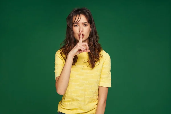 Serious young girl show silence gesture to keep secret private information on green studio background. Privacy concept — 图库照片