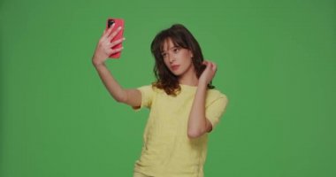 Güzel genç kız blogcu, krom yeşil arka plandaki sosyal ağ içeriği için telefonda selfie çekiyor..