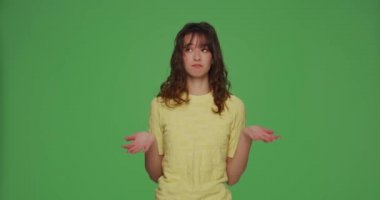 Şaşkın genç kız, krom yeşil arka planda şaşkın omuzlarını silkti. İkilem, bilmiyorum.