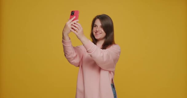 Портрет Сельфі. Усмішка щаслива дівчина робить самовідтворення, зображуючи, використовуючи смартфон на жовтому фоні. — стокове відео