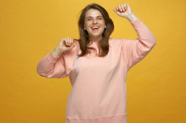 Neşeli, enerjik 20 'li yaşlardaki genç kız ellerini kaldırarak atlıyor, gülüyor, sarı arka planda eğleniyor. Pozitif duygular