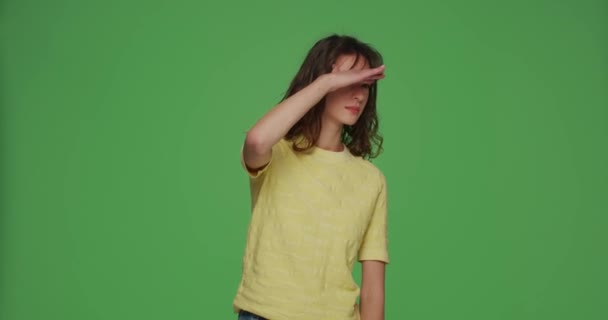 Menina atenciosa focada olhando ao redor com a mão sobre a testa, pesquisa, detectar encontrar no fundo verde chromakey — Vídeo de Stock