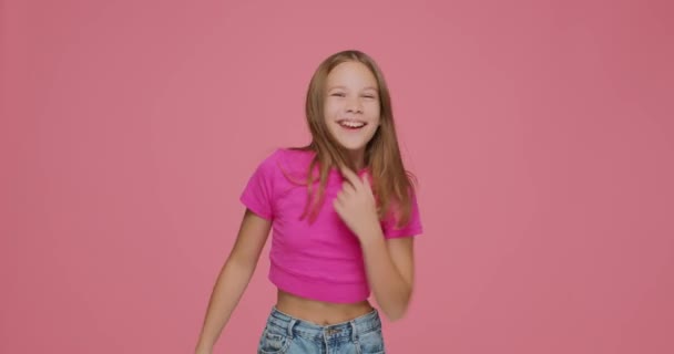Танцююча мила дівчинка крута рухається, розважається, посміхається, святкує досягнення, насолоджується музикою на рожевому студійному фоні — стокове відео