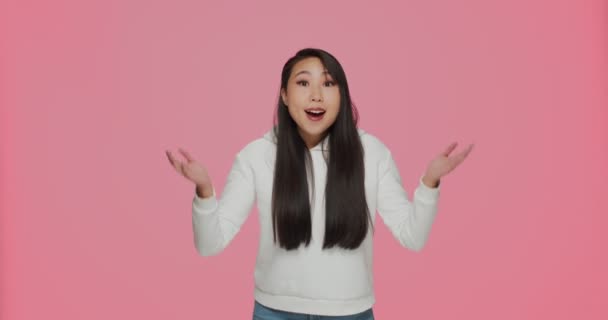 Возбужденная счастливая азиатская молодая девушка восклицает вау удивлен невероятным предложением интернет-магазина, раскинув руки на розовый фон — стоковое видео