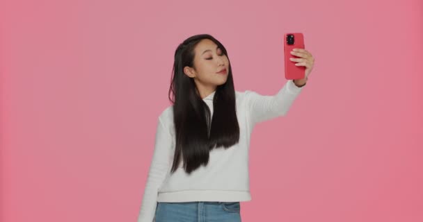 Bastante joven asiático chica blogger posando haciendo selfie disparo en móvil para social red contenido en rosa fondo — Vídeo de stock