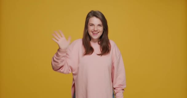 Un gesto de bienvenida. Sonriente amigable niña hospitalaria agitando las manos, saludo con los suscriptores en el fondo amarillo — Vídeos de Stock