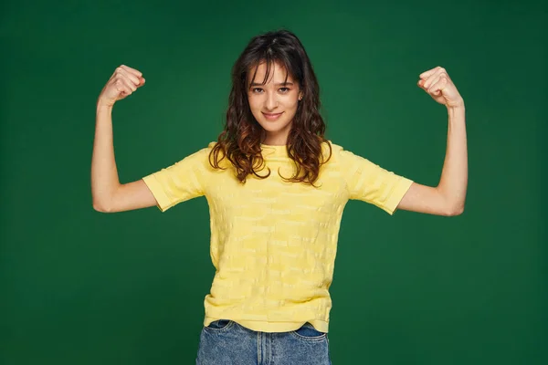 Hezká mladá dívka ukázat ruce svaly, moc, pocit hrdosti na úspěchy, udržuje fit a zdravé na zeleném pozadí — Stock fotografie