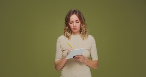 Ευσεβής νεαρή γυναίκα σκέφτεται πάνω από έξυπνη ιδέα, να γράψει σχέδια, να κάνει λίστα σε σημειωματάριο στο πράσινο φόντο στούντιο — Αρχείο Βίντεο